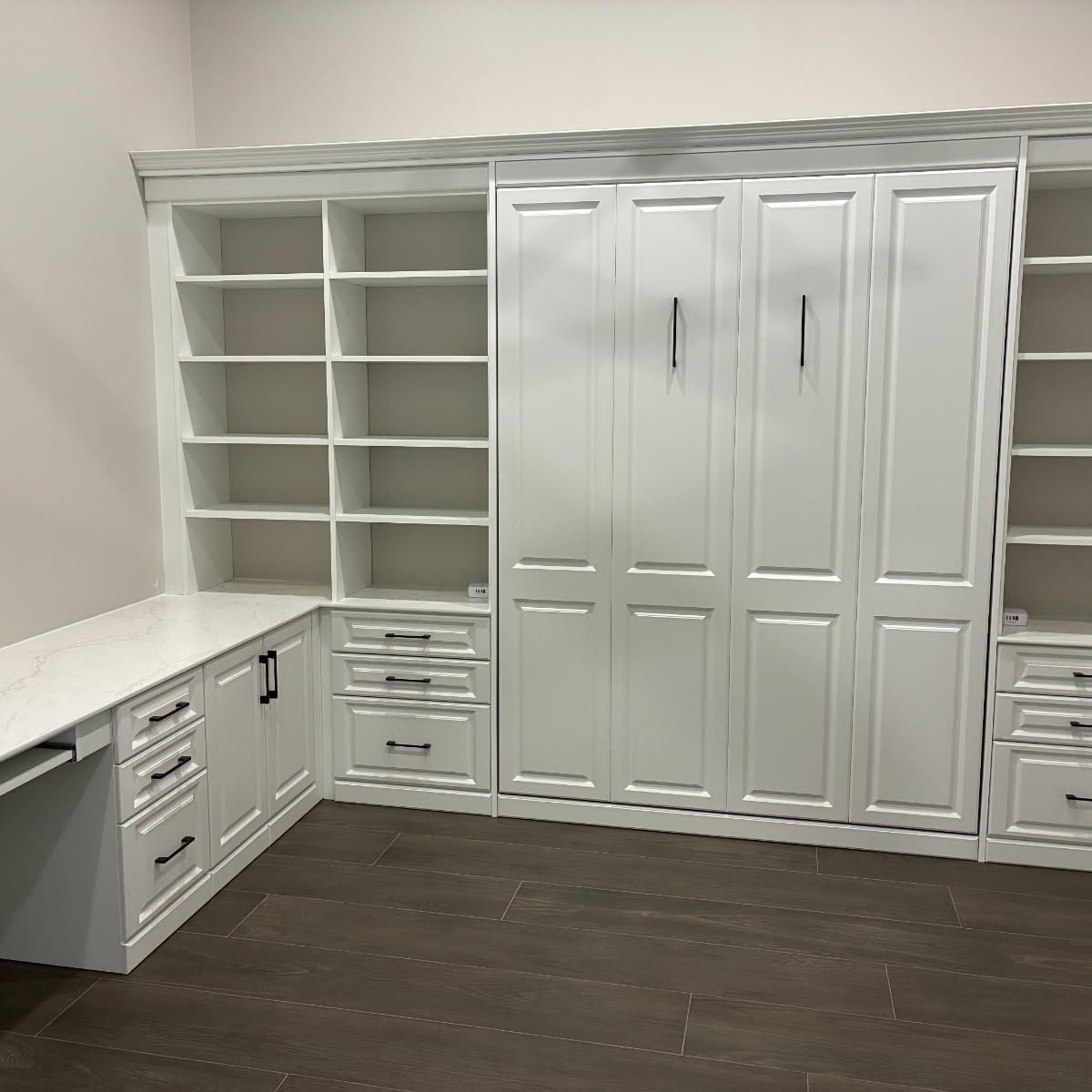 White murphy bed and home office combination with L-shaped quartz desk, raised-panel cabinetry, and open bookcase shelving