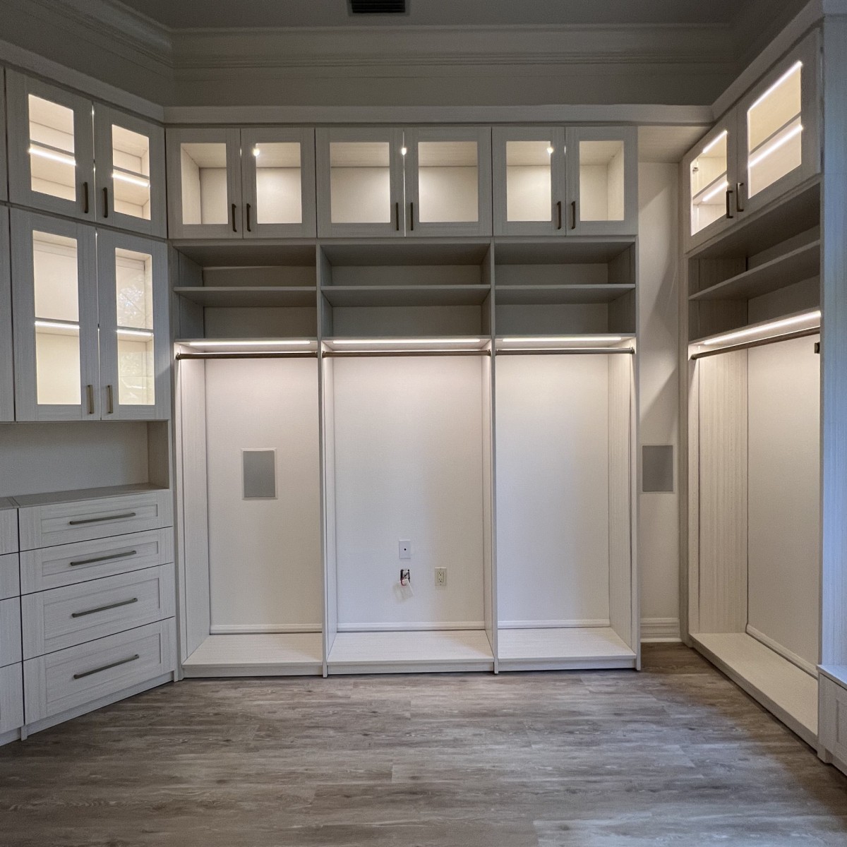 Luxury walk-in closet with shaker white cabinetry, lit glass-front upper cabinets, triple hang section, and chandelier, More Space Place Florida