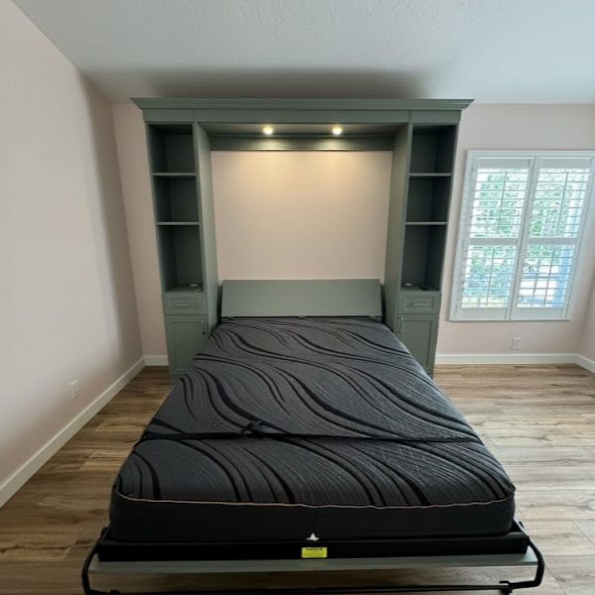 Celadon green murphy wall bed open with puck lighting, shaker cabinet surround, and integrated side shelving