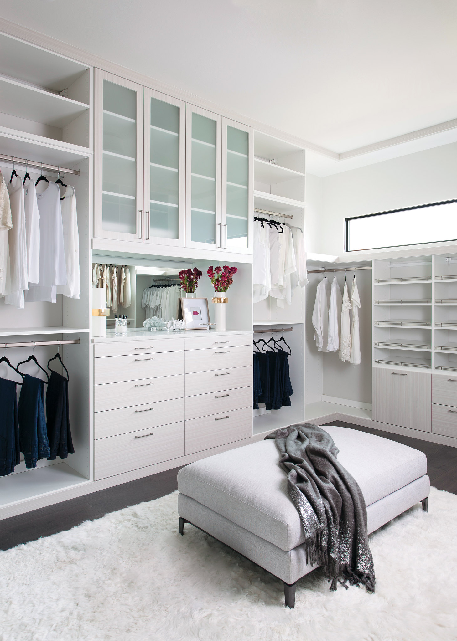 Large walk-in closet with white casework, frosted glass upper cabinet doors, full-length mirror, multi-drawer dresser tower, double hang rods, and accessory shelving