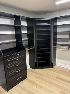 Custom walk-in closet in dark espresso finish with angled corner shoe tower, open corner shelving, five-drawer base unit with raised-panel fronts and chrome bar pulls, and single-hang rod sections
